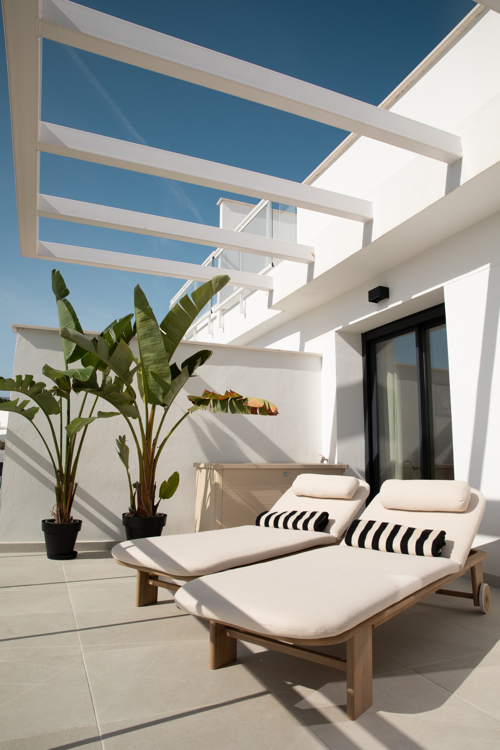Terras met ligbedden onder een pergola en palmen
